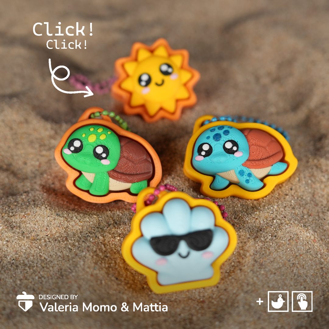 Three cute cartoon keychain charms shaped like a sun, a green turtle, and a blue turtle, displayed on a sandy surface with a 'Click! Click!' overlay and designer credit.